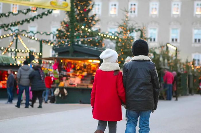 A young brother and sister walk hand in hand towards the enchanting Christmas market at Schloss Hellbrunn in Austria.