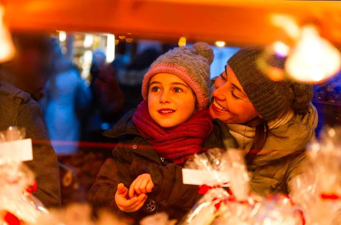 A joyful child and mother select sweets at a Christmas market in Nice, France.