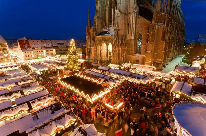 At nighttime, the Christmas market in Ulm, Germany, is set against the backdrop of its impressive Gothic cathedral.