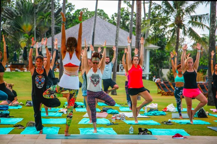 A yoga instructor leading an outdoor class and guiding students into tree pose in Bali.