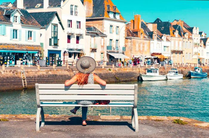 A woman sits on a bench, enjoying the view of Le Croisic village and its port in Loire-Atlantique, France.