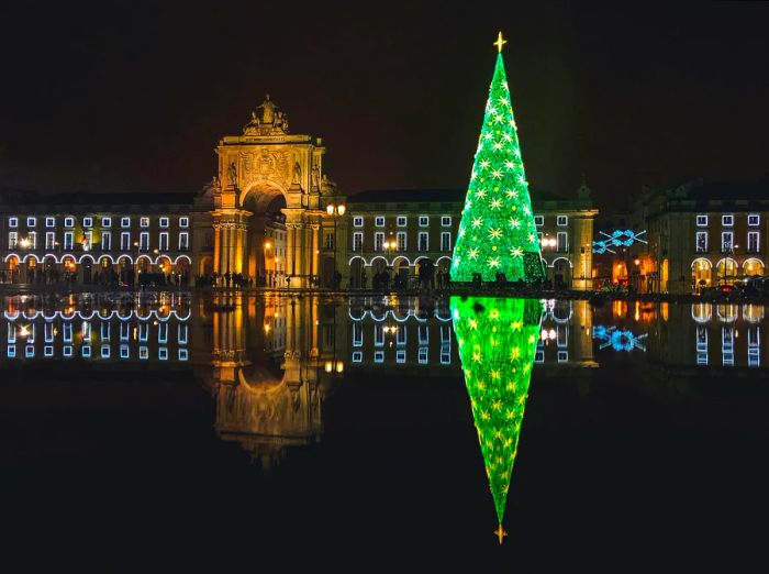 A Christmas tree adorned with decorations illuminates the night in Lisbon, Portugal, surrounded by vibrant green lights against the dark backdrop.