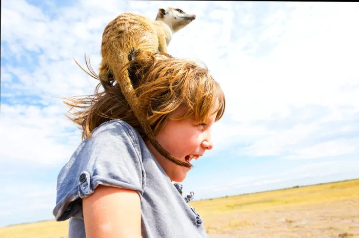 A five-year-old boy with a meerkat perched on his head in the Kalahari Desert, Makgadikgadi Salt Pans, Botswana