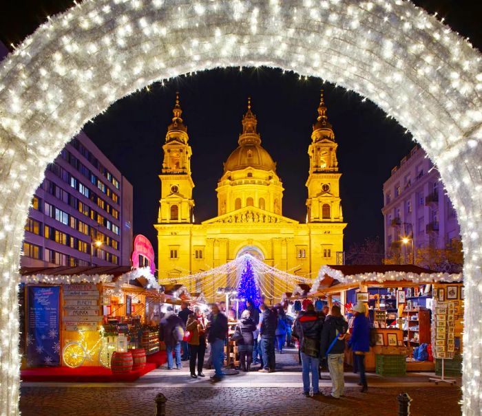 The Budapest Christmas market sparkles with lights, featuring the stunning Basilica of St Stephen in the backdrop.