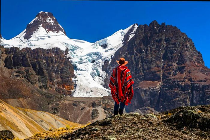 A hiker wearing a poncho stands before a majestic mountain peak