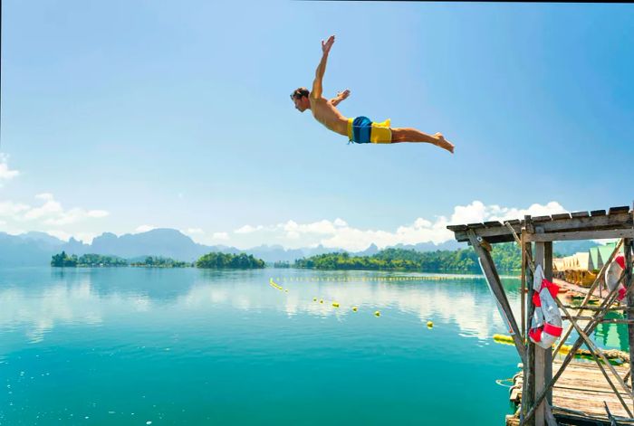 An athletic tourist jumping into the crystal-clear waters of Lake Ratchaprapha, Khao Sok National Park