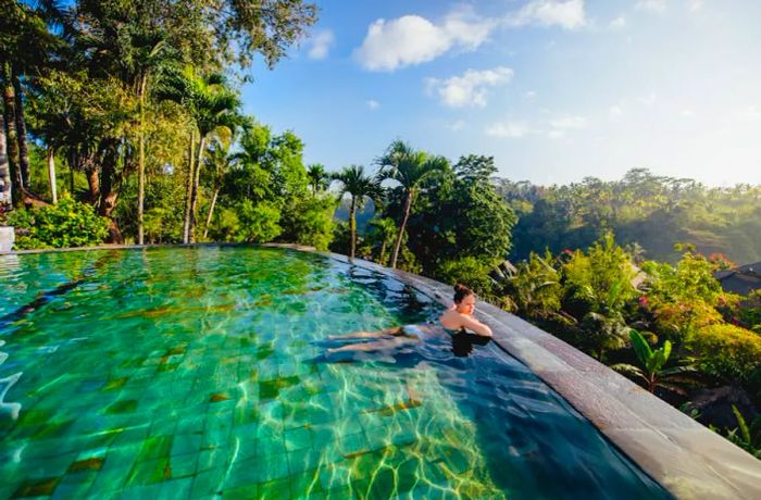 A woman enjoys the view of a lush valley from the edge of an infinity pool © bogdanhoda / Shutterstock