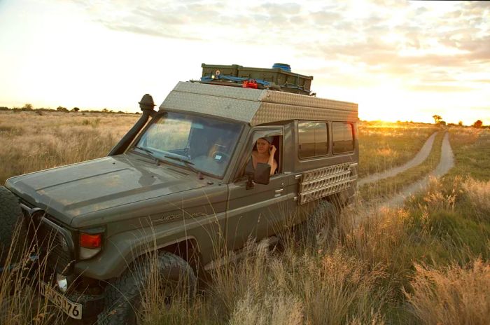 A Land Cruiser navigates the bush in Botswana, following a dirt path with a woman inside