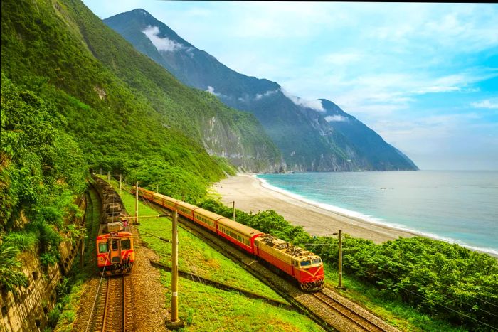 Two trains travel along a lush green coastline with a tall mountain in the background