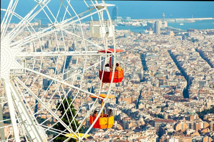 An overhead shot of a Ferris wheel adorned with vibrant cars, offering stunning views of Barcelona.