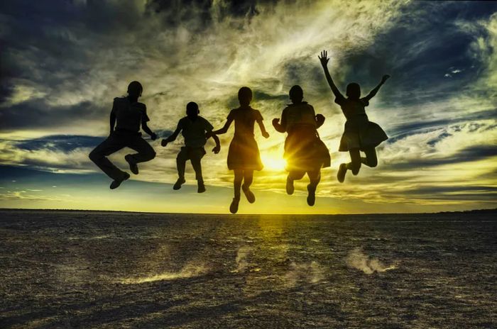 A group of African children joyfully jumping against the backdrop of a sunset in Botswana