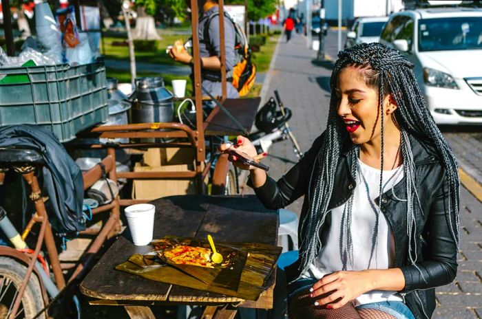 A woman captures a photo of her meal from a nearby street food vendor