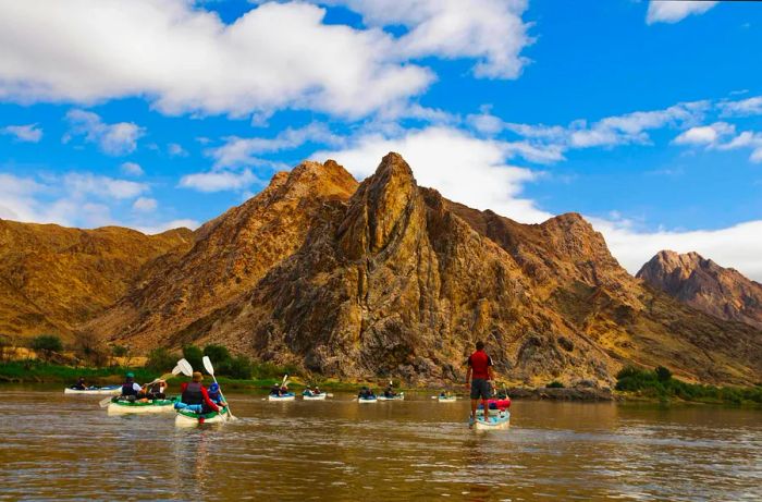 People kayaking along a river with towering rocky peaks in the surrounding landscape