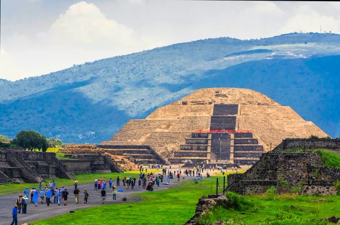 Tourists stroll along a path leading to a grand stone pyramid