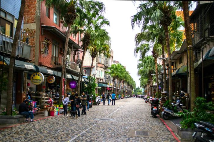 People and scooters navigate Yingge Ceramics Old Street, lined with towering palm trees and historic buildings.