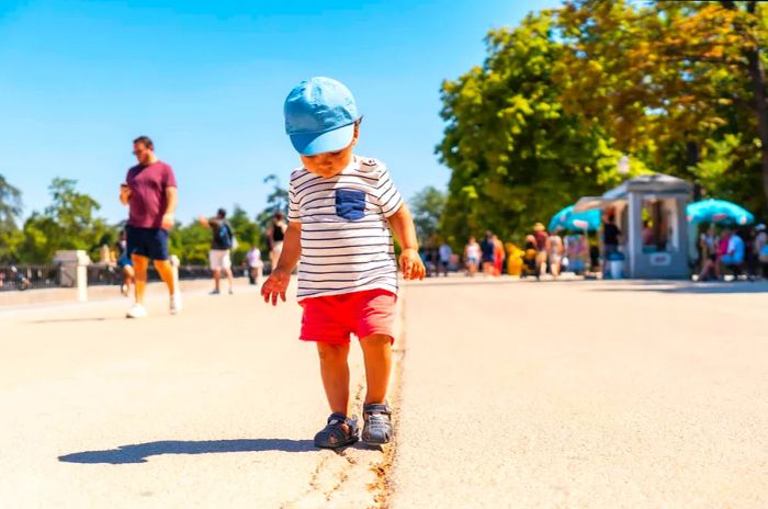 A toddler focuses intently as he walks along a line drawn on the ground in a park.