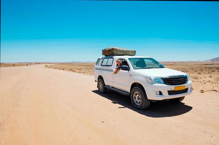 A man drives a four-wheel vehicle with a rooftop tent, parked along a dusty desert road