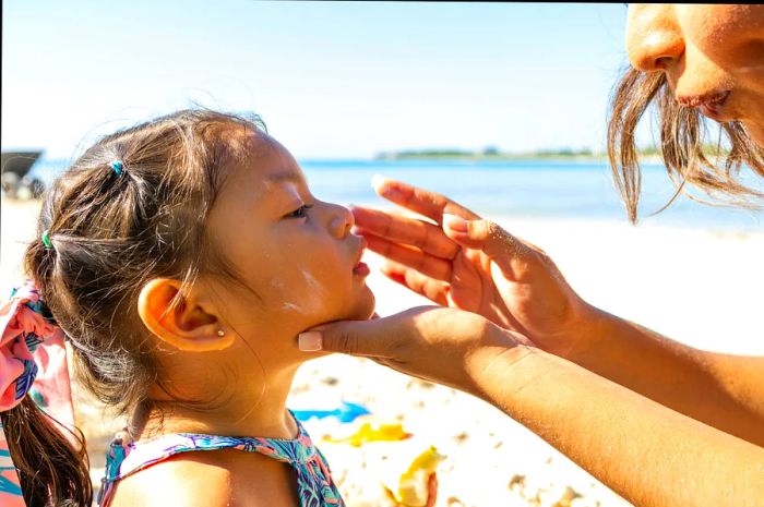 A mother applies sunscreen on her young daughter's face