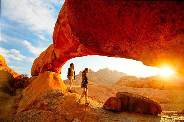 A father and daughter enjoying the sunrise in the Spitzkoppe area, surrounded by picturesque stone arches and unique rock formations in Damaraland, Namibia