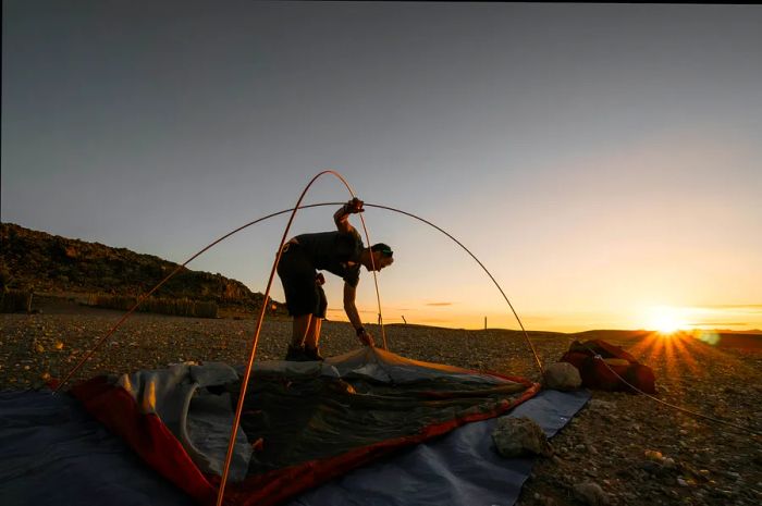 A person pitches their tent in a secluded area of the African bush as the sun sets