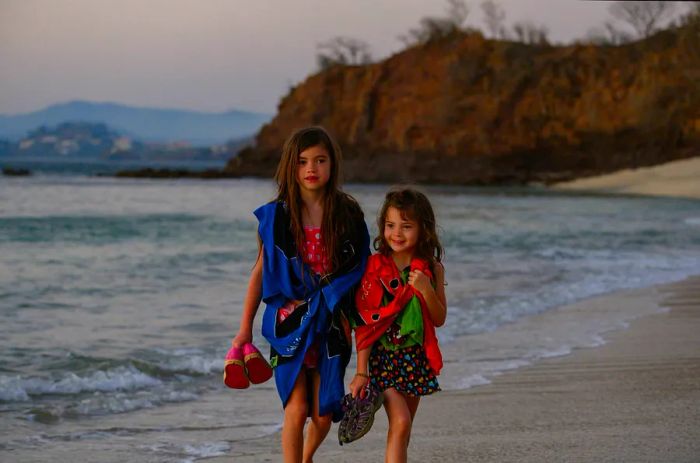 Two young girls stroll together along a beach in Central America.