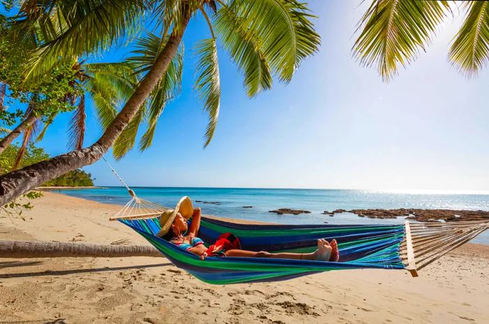 Woman relaxing with headphones on a hammock at the beach, Kadavu Island, Fiji