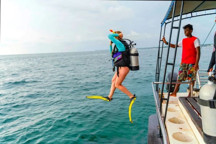 A diver in a wetsuit and aqualung leaping into the sea from a boat