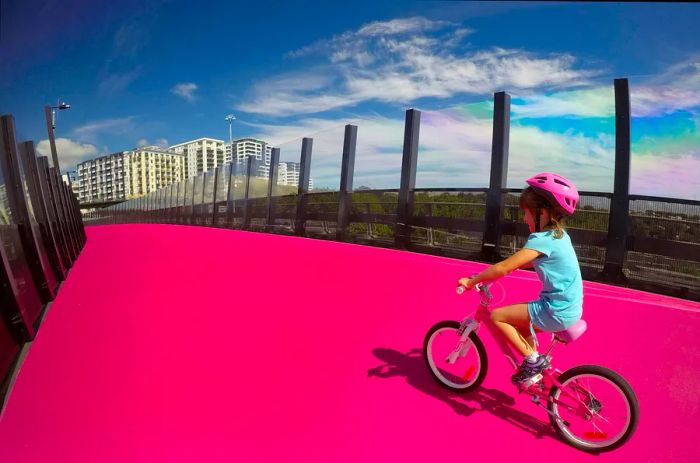 A young girl (aged 7) rides her bike along a vibrant pink cycleway in Auckland, New Zealand.