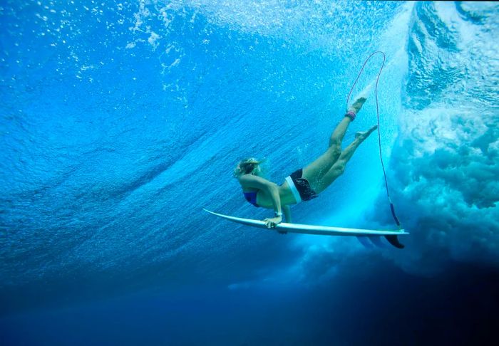 A female professional surfer glides through the waves with her board at Cloud Break, Fiji.