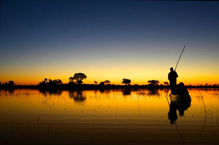 A canoe glides quietly at dusk over the waters of the Okavango Delta in Botswana.