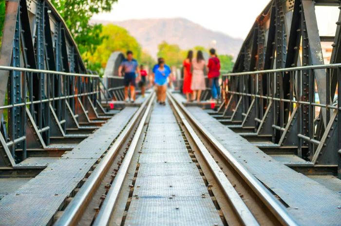 A crowd of people walking alongside the railway of the old railroad bridge over the River Kwai in Kanchanaburi, Thailand.