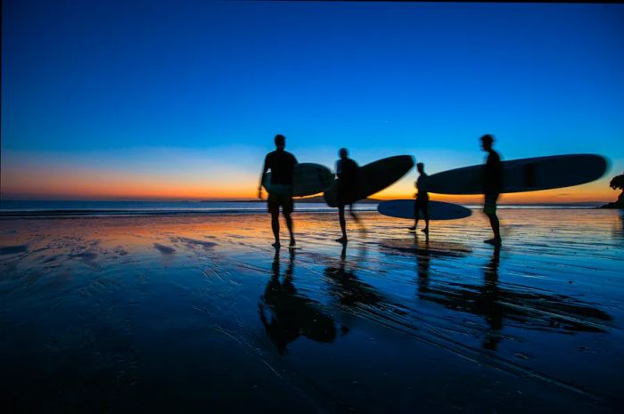 Surfers silhouetted against a stunning pink-and-blue sunrise at Takapuna Beach.