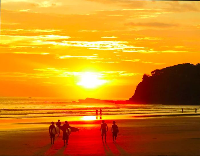 Surfers and beachgoers admire the golden-orange sunset at Playa Hermosa, Nicaragua