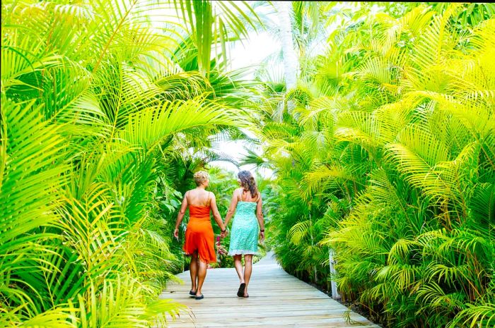 A lesbian couple holding hands on a tropical walkway