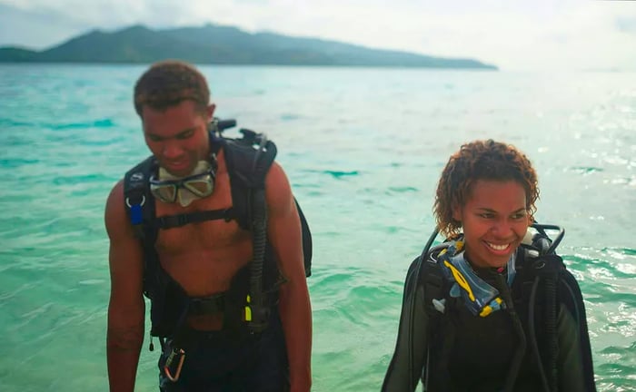 A pair of scuba divers happily emerge from the ocean in Fiji