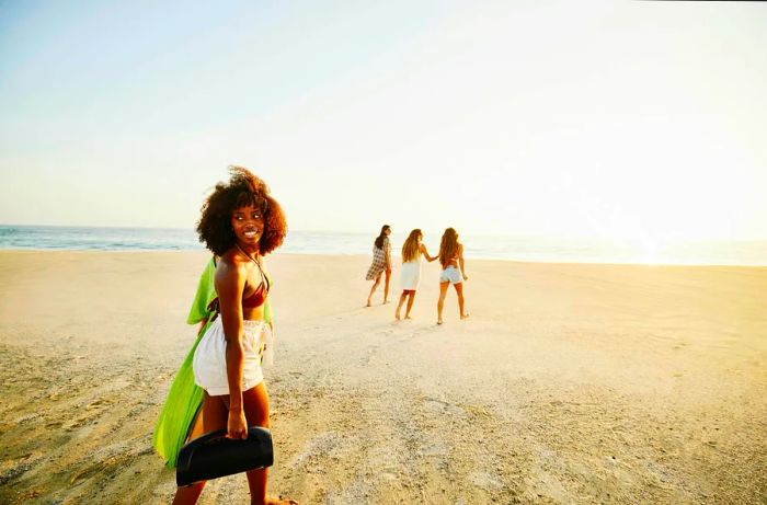 A woman walks along the beach in Mexico with a speaker, her friends slightly ahead of her