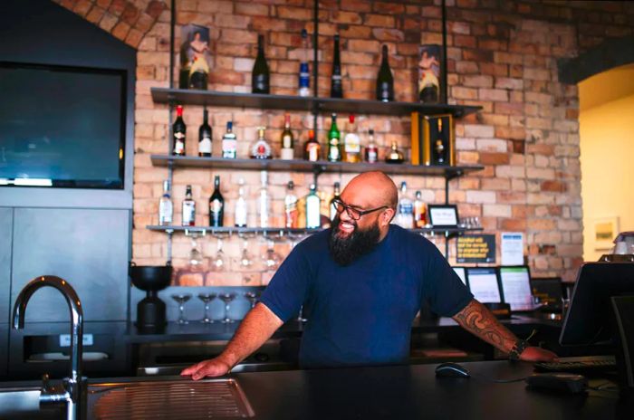 A bartender stands smiling at the bar, hands resting on it