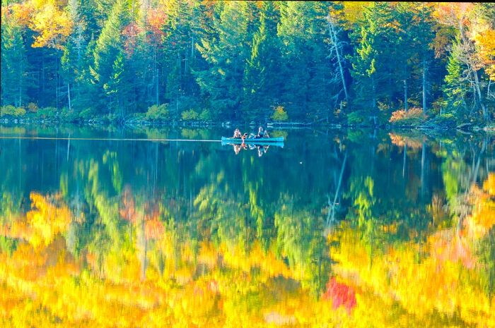 A canoe glides through the vivid yellow reflections of autumn foliage on Grout Pond in the Green Mountain National Forest, Vermont.