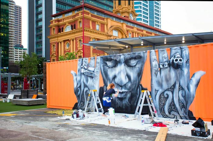 An artist paints a mural on a train car.