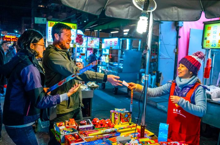 Two individuals happily exchange money with a vendor at a night market stall