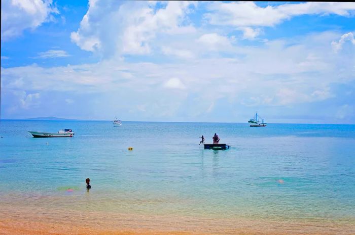 Gazing out at the water, people and boats enjoy the crystal-clear tropical sea, with Big Corn Island visible on the horizon.