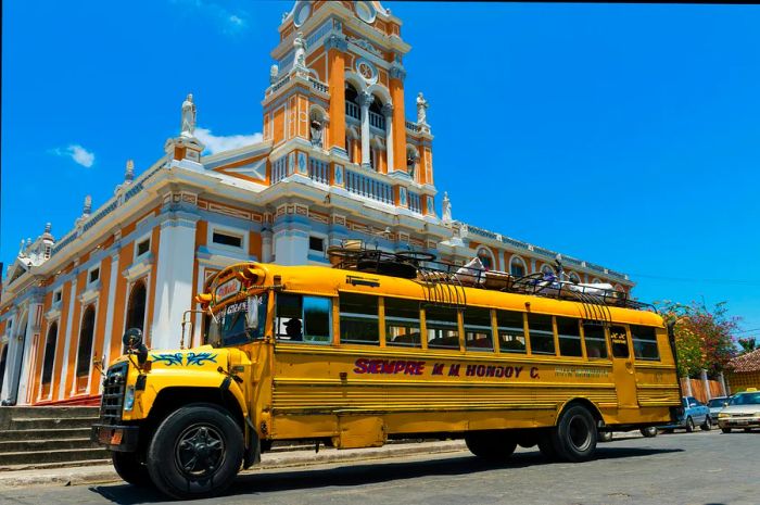 A yellow bus parked in front of a church in Granada, Nicaragua