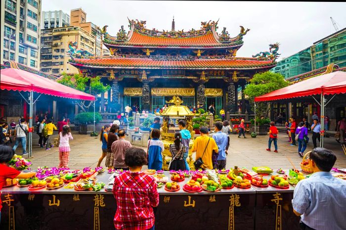 Visitors gather around tables adorned with offerings of fruit in a temple courtyard.