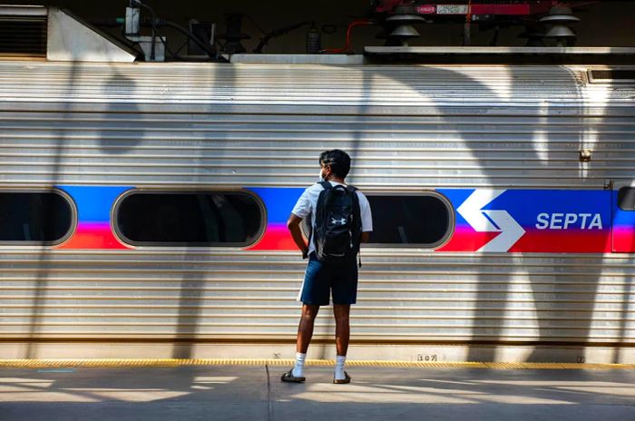 A man dressed in shorts and a backpack waits on the platform next to a SEPTA train in Philadelphia, Pennsylvania.