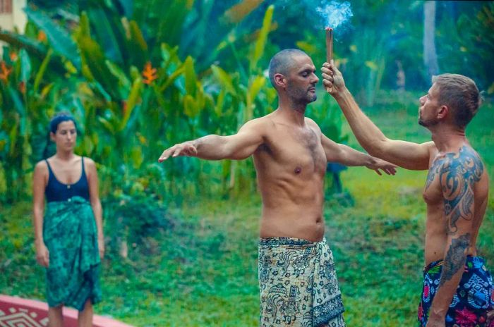 A man stands before a shaman in a jungle setting, with smoke wafting over his head during a temazcal ceremony in Mexico