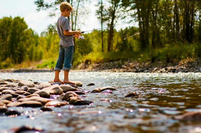 A young boy enjoys fishing in a sunlit river near Bozeman, Montana