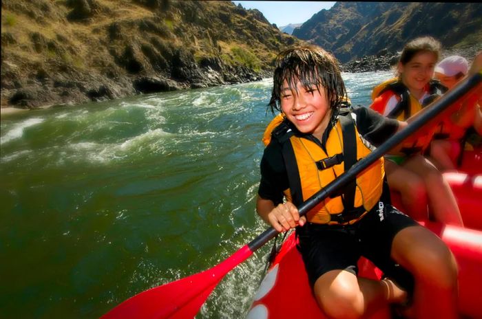 A boy beams as he rows a whitewater raft down a canyon river in the USA.