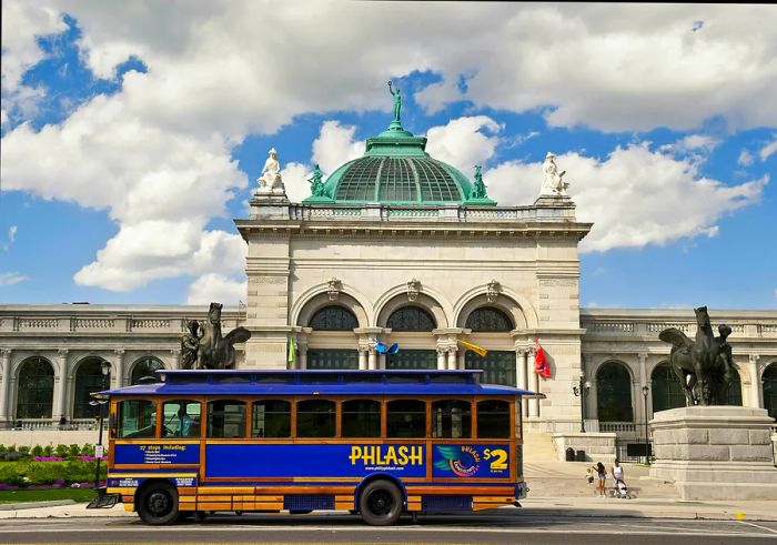 A PHLASH bus passes the Please Touch Museum on a cloudy day in Philadelphia, Pennsylvania