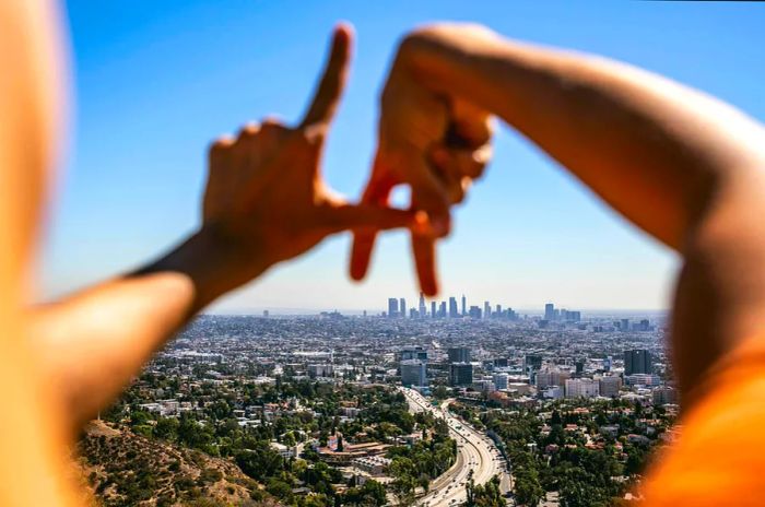 A Hispanic woman forms her hands into the shape of 'LA' while gazing across the skyline of Los Angeles.