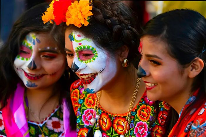 Three friends with painted faces share laughter at the Día de los Muertos Festival in Oaxaca, Mexico.